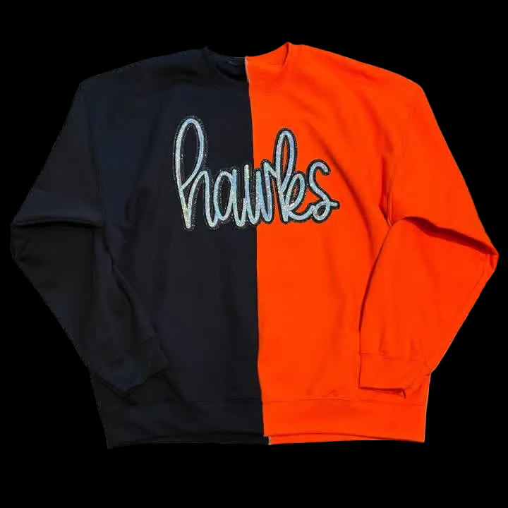 A long-sleeve crewneck sweatshirt with a split design, featuring a black left side and a bright orange right side. The center of the chest has the word 'hawks' written in a white cursive script with a light blue outline.