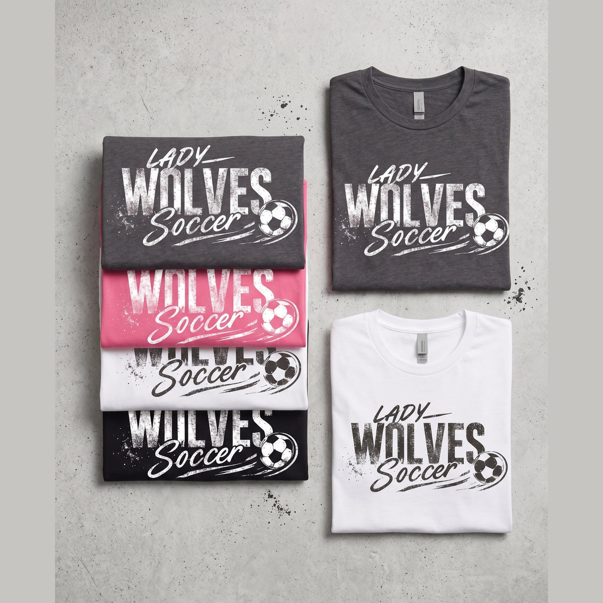 Four folded graphic T-shirts arranged on a light gray textured background. Two shirts are dark gray and two are white, each printed with the words 'Lady Wolves Soccer' and a soccer ball graphic.